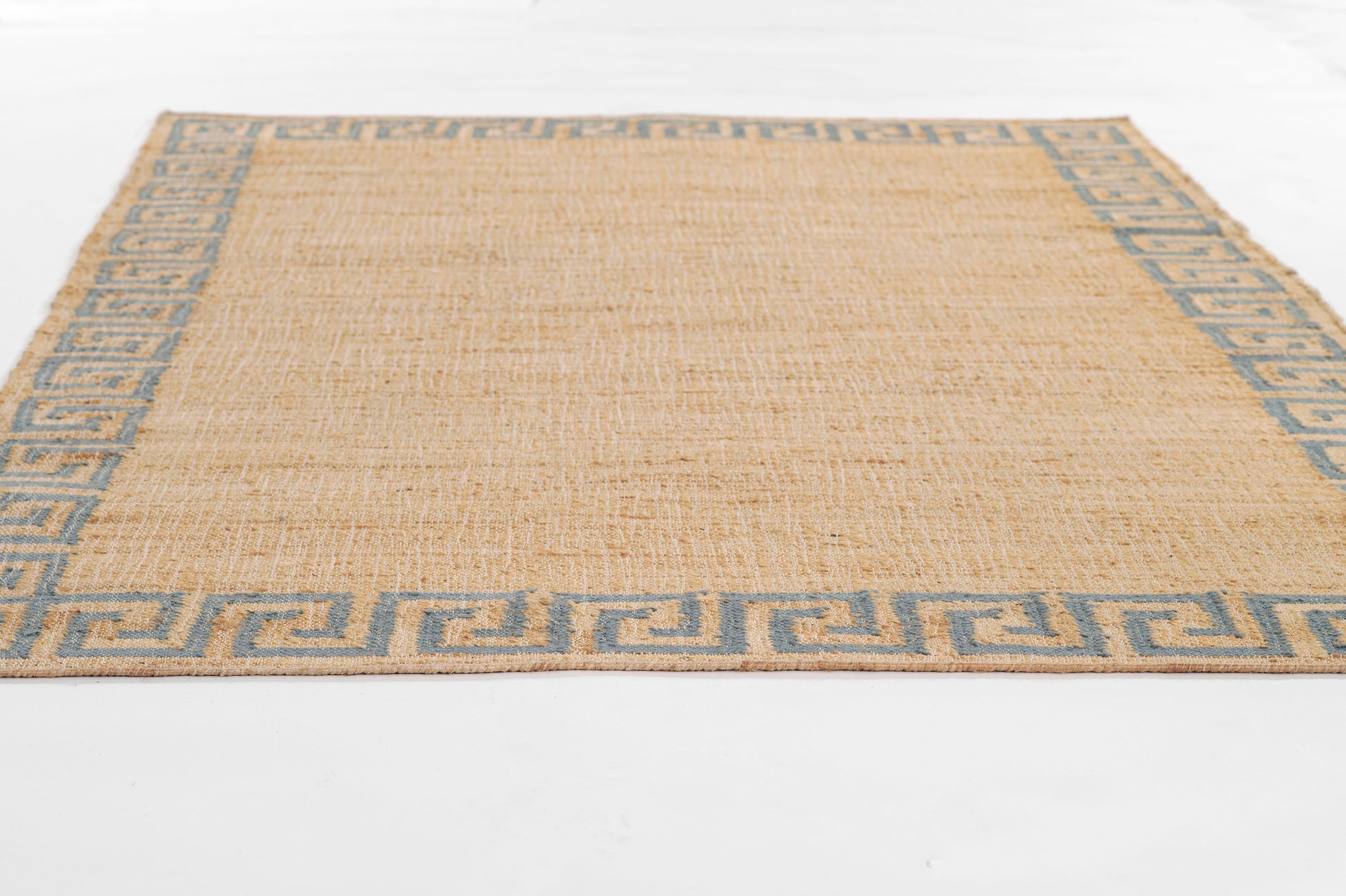 Woven natural jute rug with blue Greek-key border; rectangular, coastal style.
