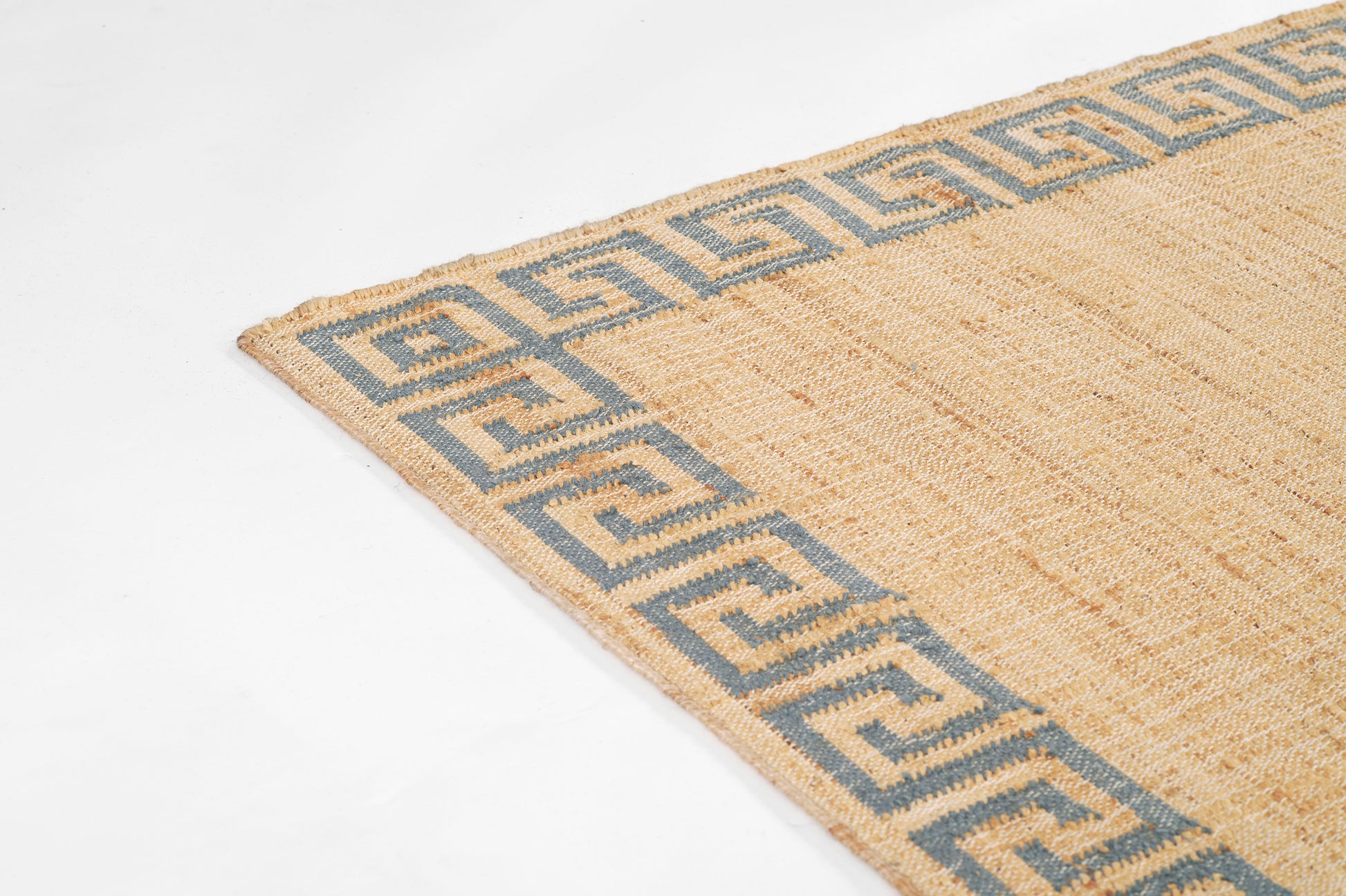 Beige jute rug with blue Greek key border along edges; textured woven surface.
