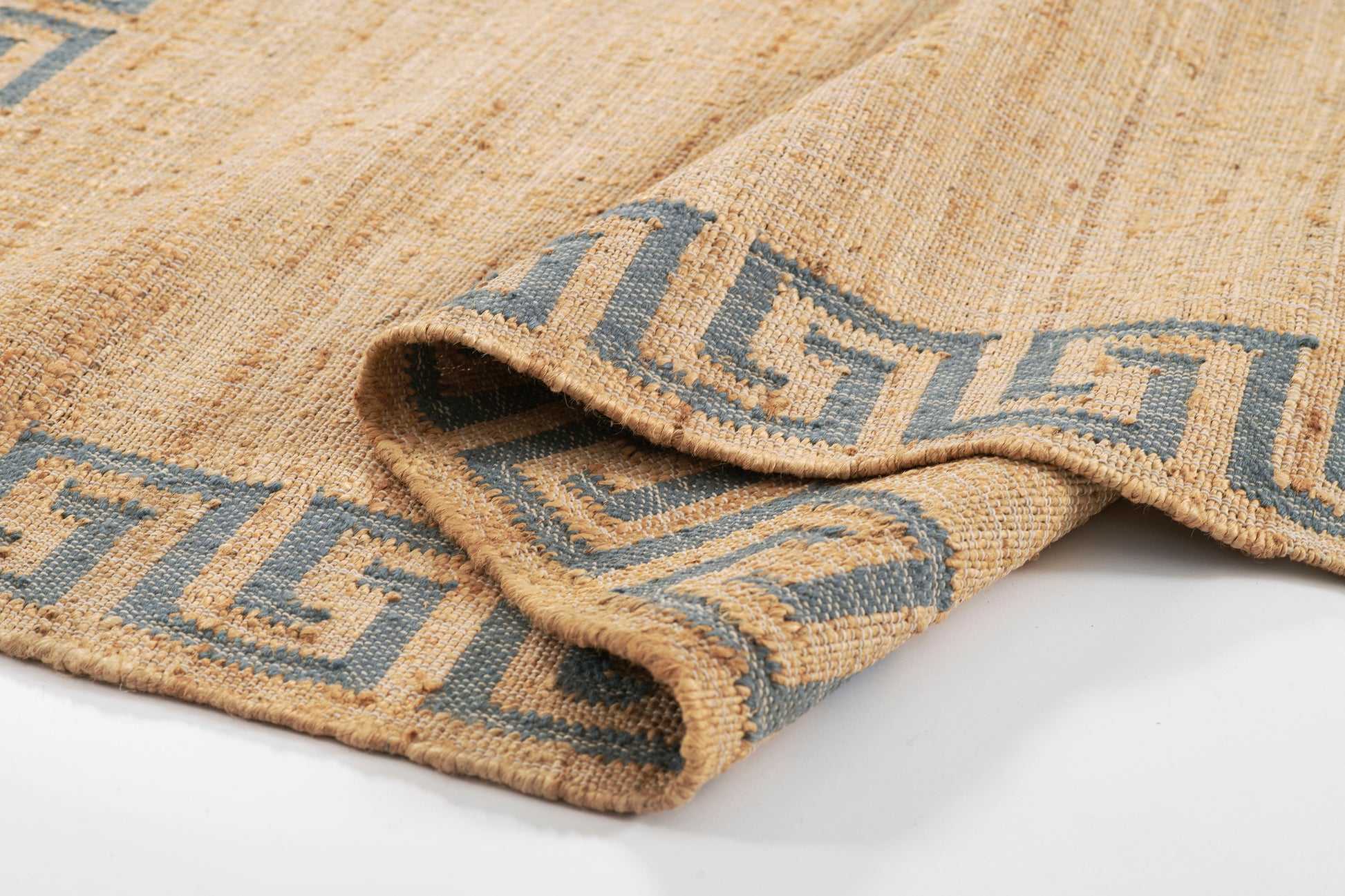Beige jute rug with blue Greek key border, folded to reveal textured woven surface.