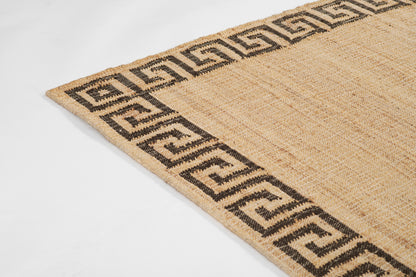 Beige jute rug with black Greek key border, textured natural fiber, rectangular shape, rustic coastal style.