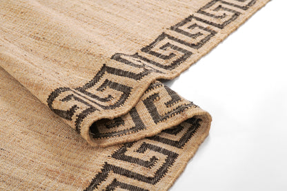 Beige natural fiber rug with a dark brown Greek-key border, folded to reveal thick woven texture.