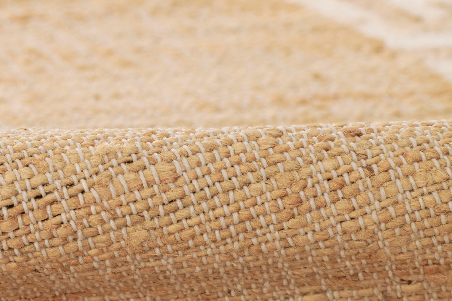 Close-up of a natural beige woven jute rug with white thread accents and a rolled edge.
