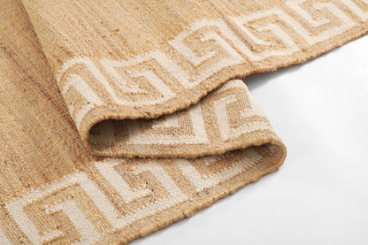Beige woven rug with white Greek key border; natural jute-like texture, folded edge.