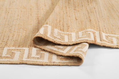 Beige woven rug with cream Greek key border, folded edge showing textured fibers.