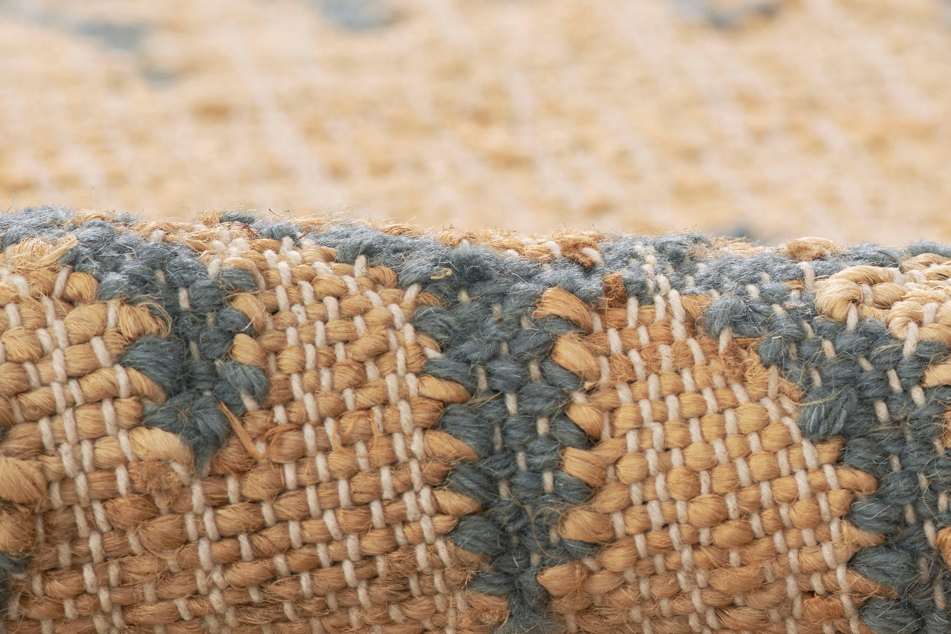 Close-up of a woven natural fiber rug with tan and blue-gray stripes and chunky textured weave.