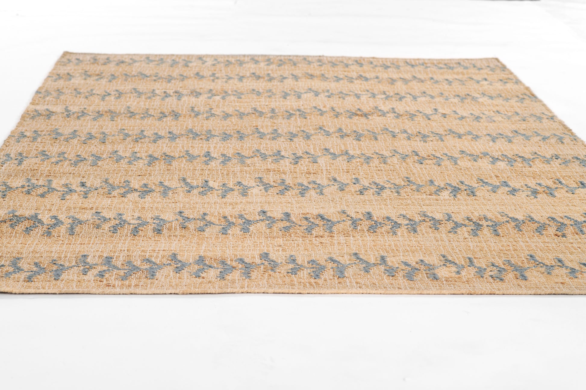Rectangular flat-weave rug in natural beige with blue geometric motifs; rustic jute texture.