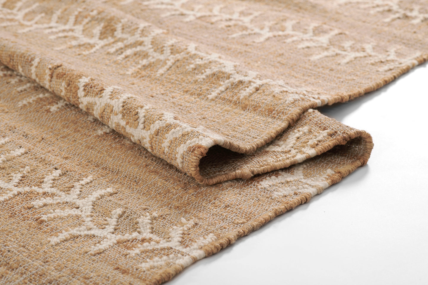 Beige woven rug with cream leaf-like pattern, soft textured pile, folded edge for close-up view.