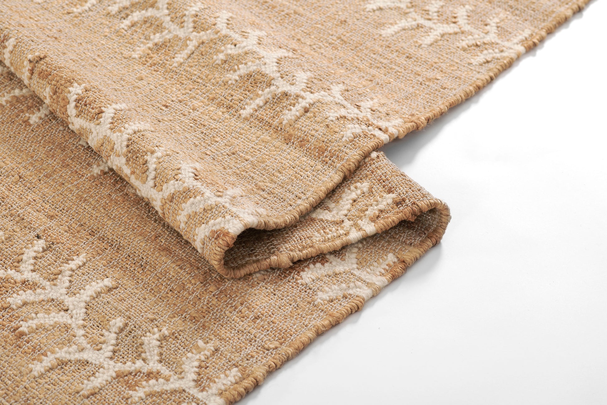 Beige woven rug with white vine stripe pattern; natural fiber texture and folded corner.