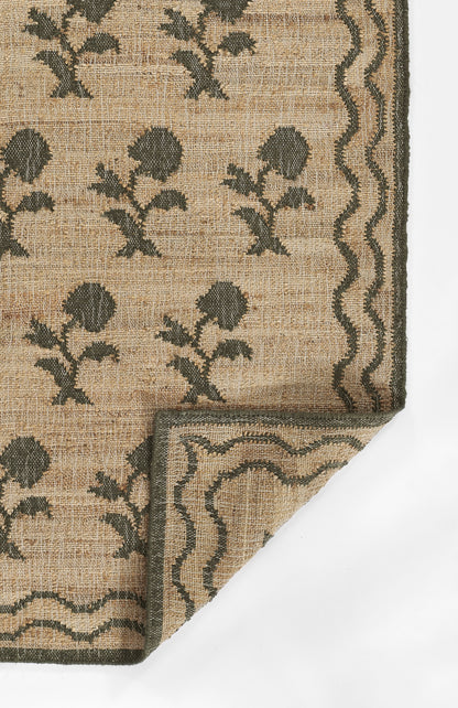 Beige woven rug with dark green floral motifs and a wavy border; folded corner reveals layered edge.