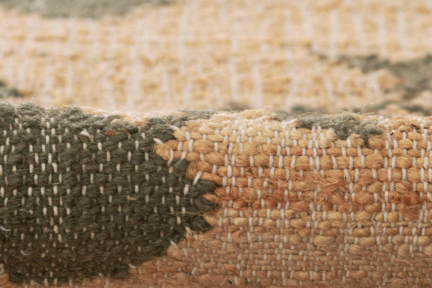 Close-up of a two-tone woven jute rug—dark green and natural beige—with textured fibers and a folded edge.