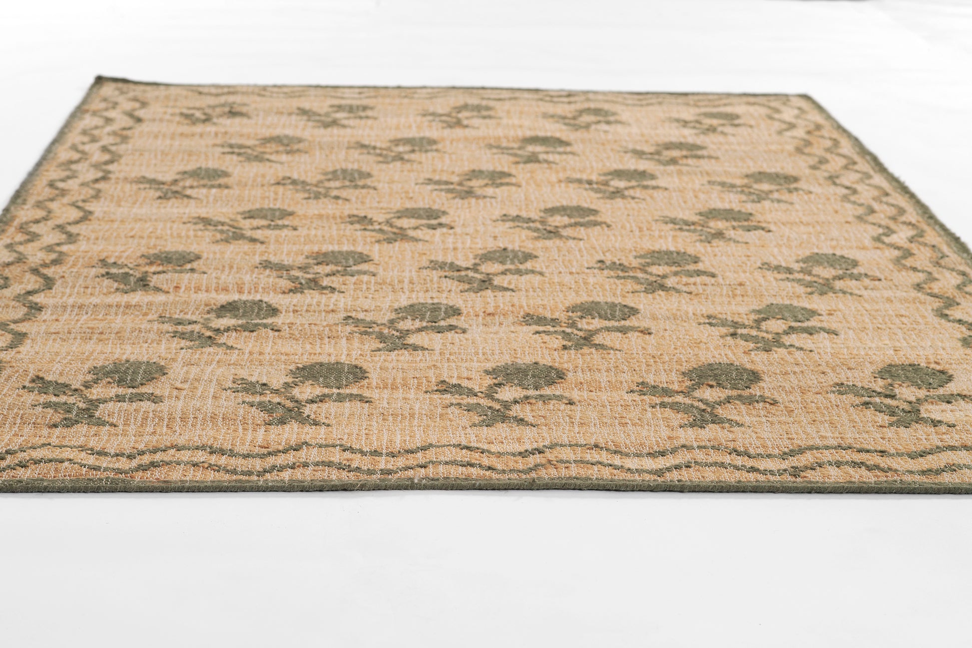 Rectangular beige flatwoven rug with olive-green flower motifs, dark border; natural fiber coastal style decor.