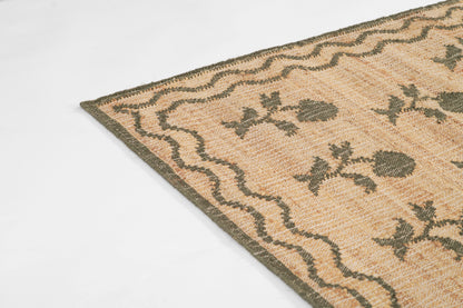 Beige woven rug with green floral motifs and a wavy border, close-up corner view.