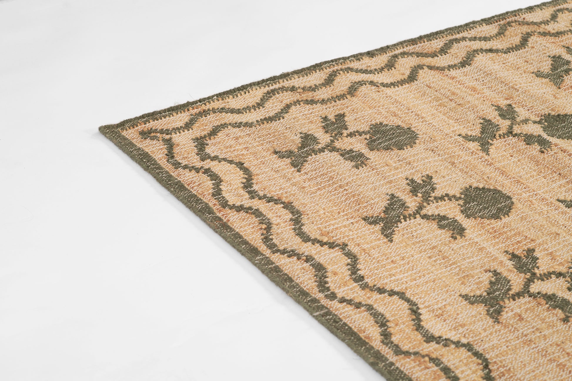 Beige woven rug with dark green floral motif and wavy border; corner view.