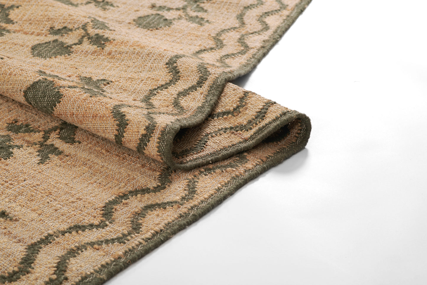 Beige rug with olive-green floral geometric pattern, folded edge showing soft woven texture.