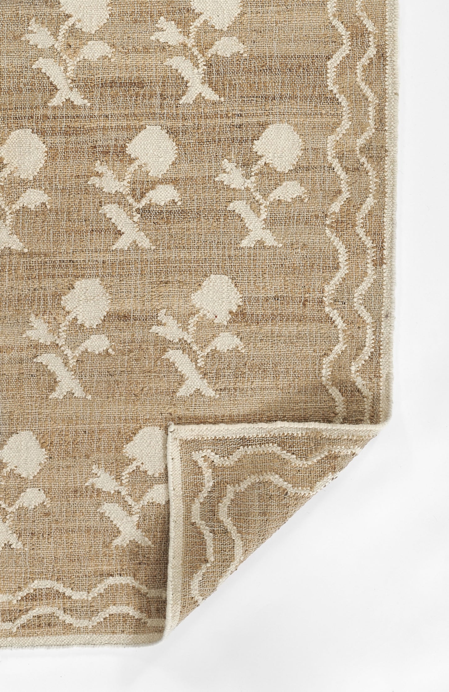 Natural beige jute-like rug with ivory floral motifs and a white wavy border; rectangular, folded corner shows backside.