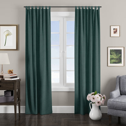 Emerald teal curtains frame a bright window in a cozy living room with a side table, lamp, art, gray sofa, and pink flowers.