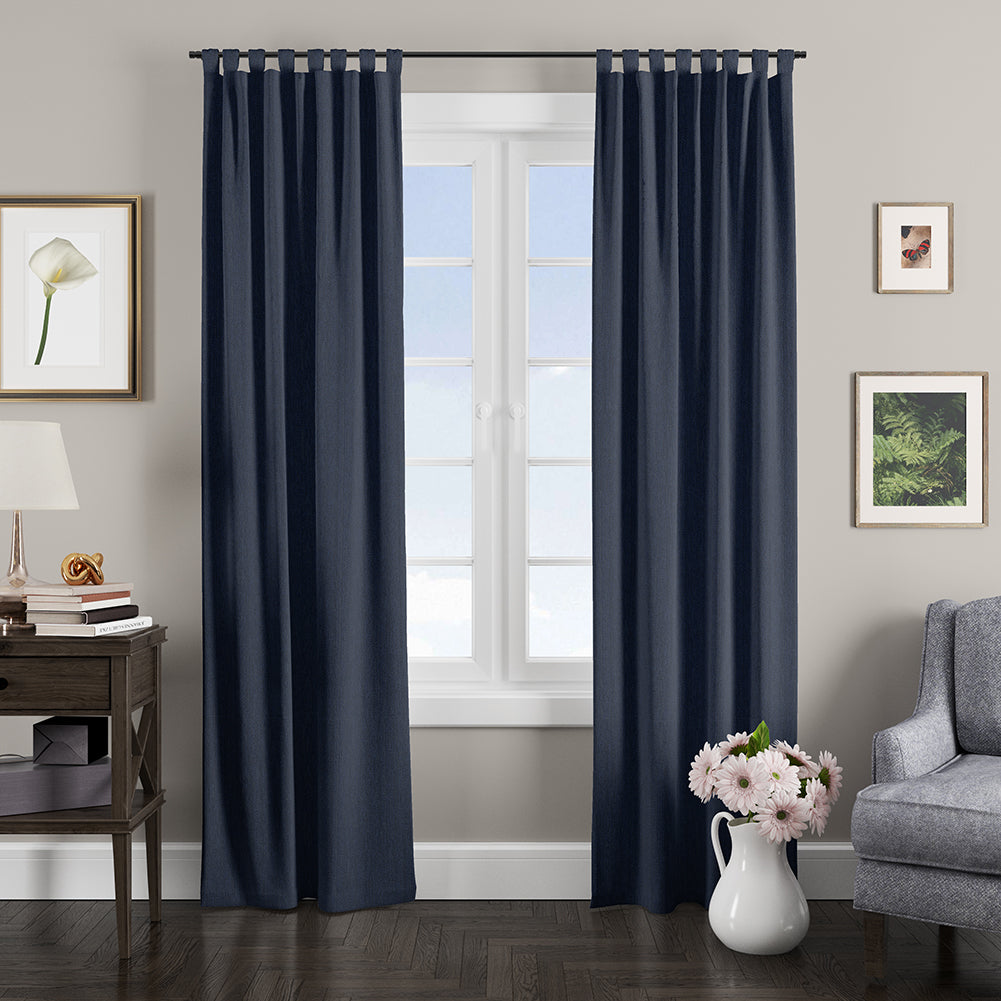 Floor-length navy blue curtains on a metal rod in a gray living room with a wooden console, lamp, framed art, a gray armchair and a pink bouquet vase.