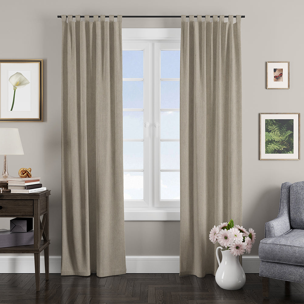 Taupe grommet-top curtains frame a white window in a neutral living room with a wood side table, lamp, art, and pink flowers.