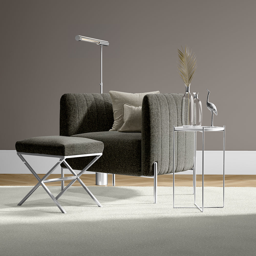 Dark gray tufted armchair with chrome legs & matching ottoman, glass side tables, floor lamp, dried palm decor—modern lounge.