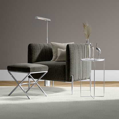 Dark gray tufted armchair with chrome legs & matching ottoman, glass side tables, floor lamp, dried palm decor—modern lounge.