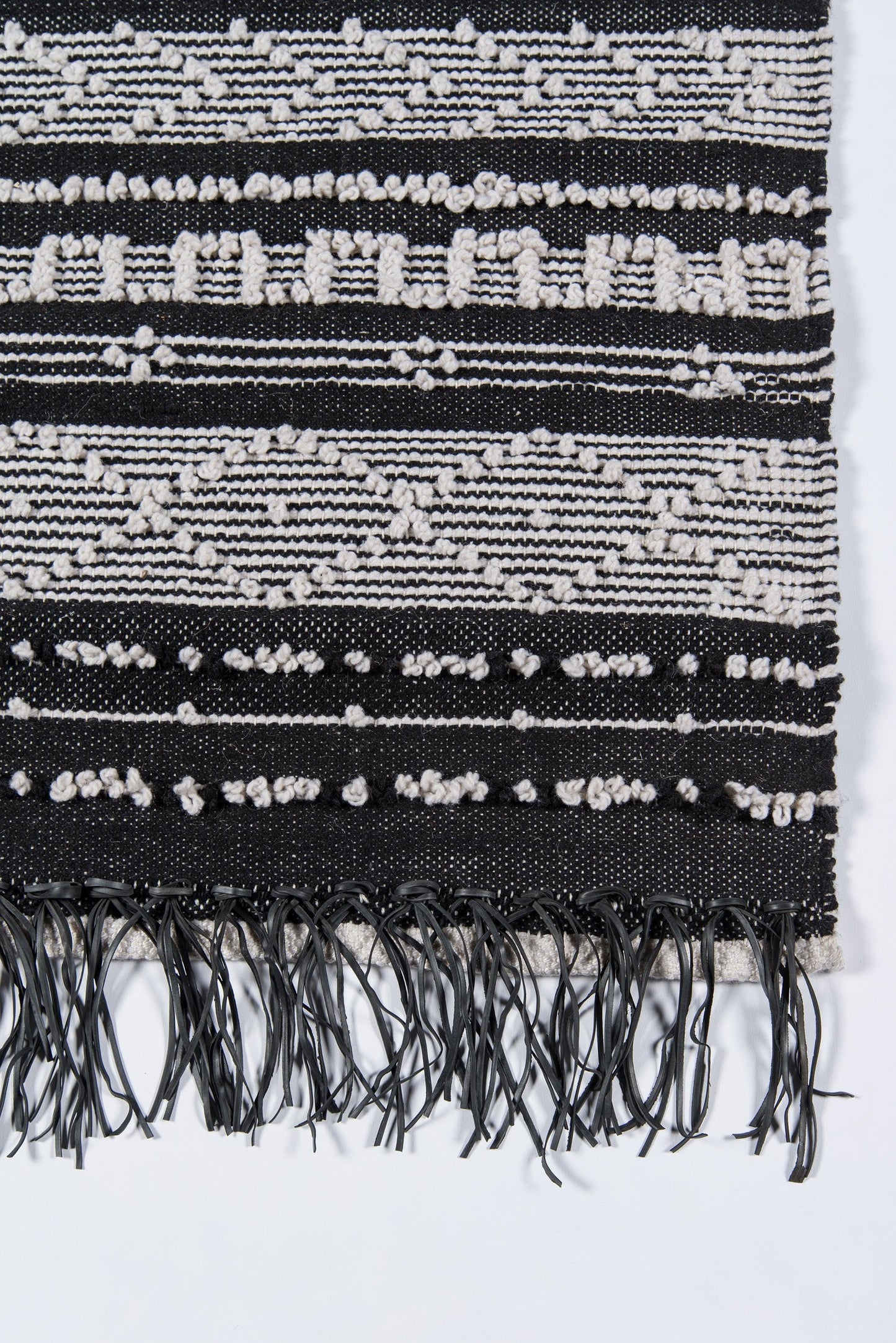 Black and white woven rug with geometric stripes, diamond motifs, and fringed ends.