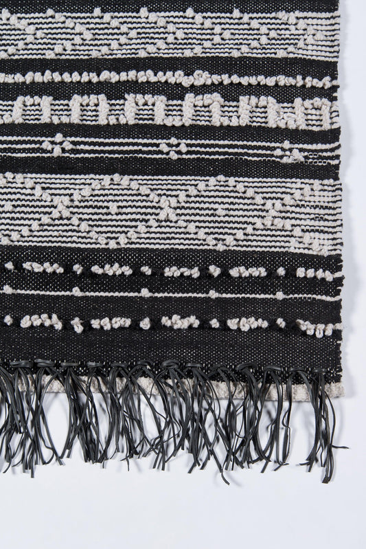Black and white woven rug with geometric stripes, diamond motifs, and fringed ends.