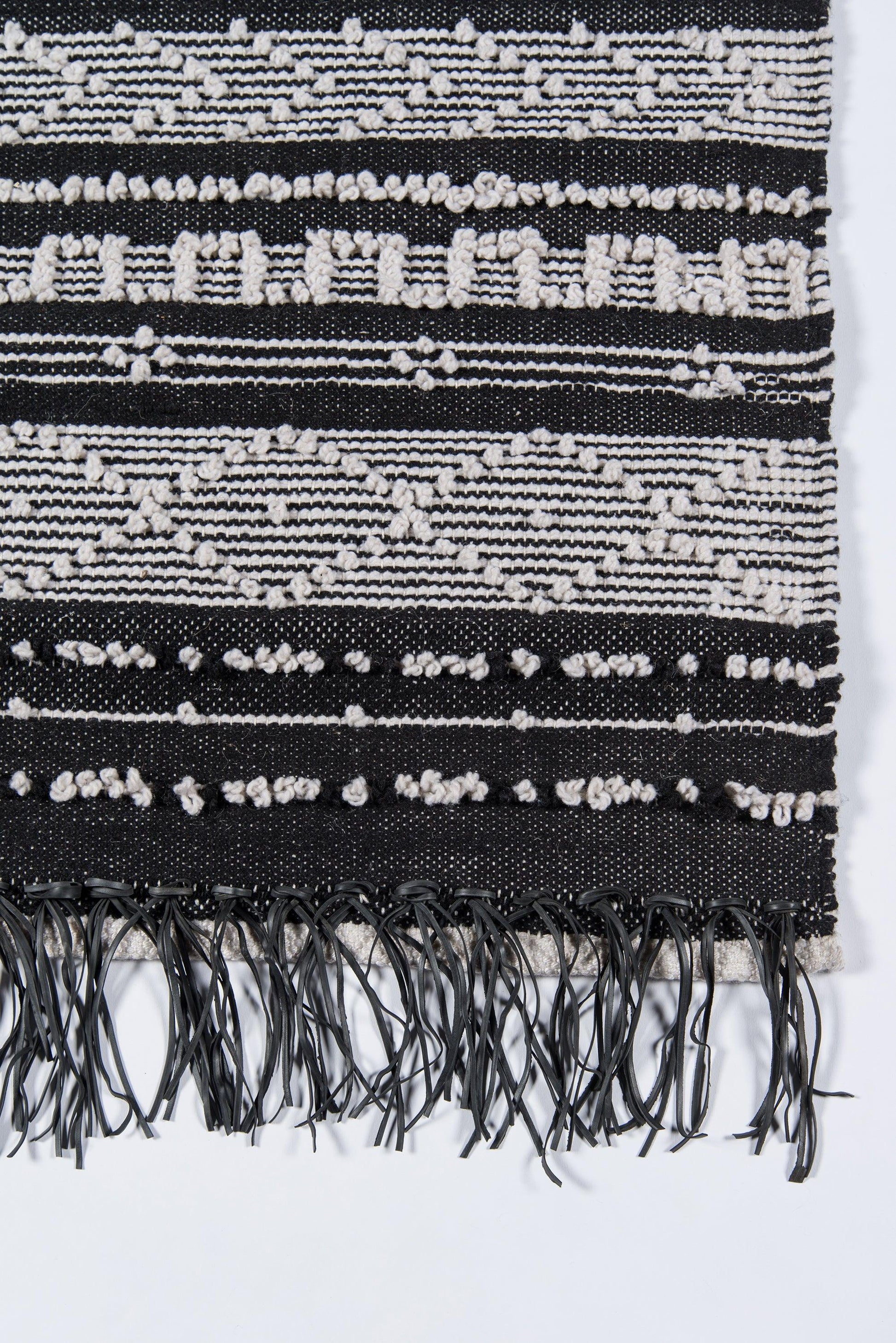 Black and white woven textile with geometric stripes and fringe tassels along bottom edge.