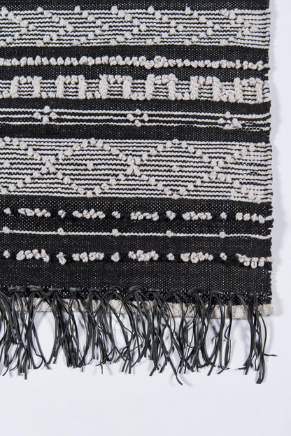 Black and white woven textile with geometric stripes and fringe tassels along bottom edge.