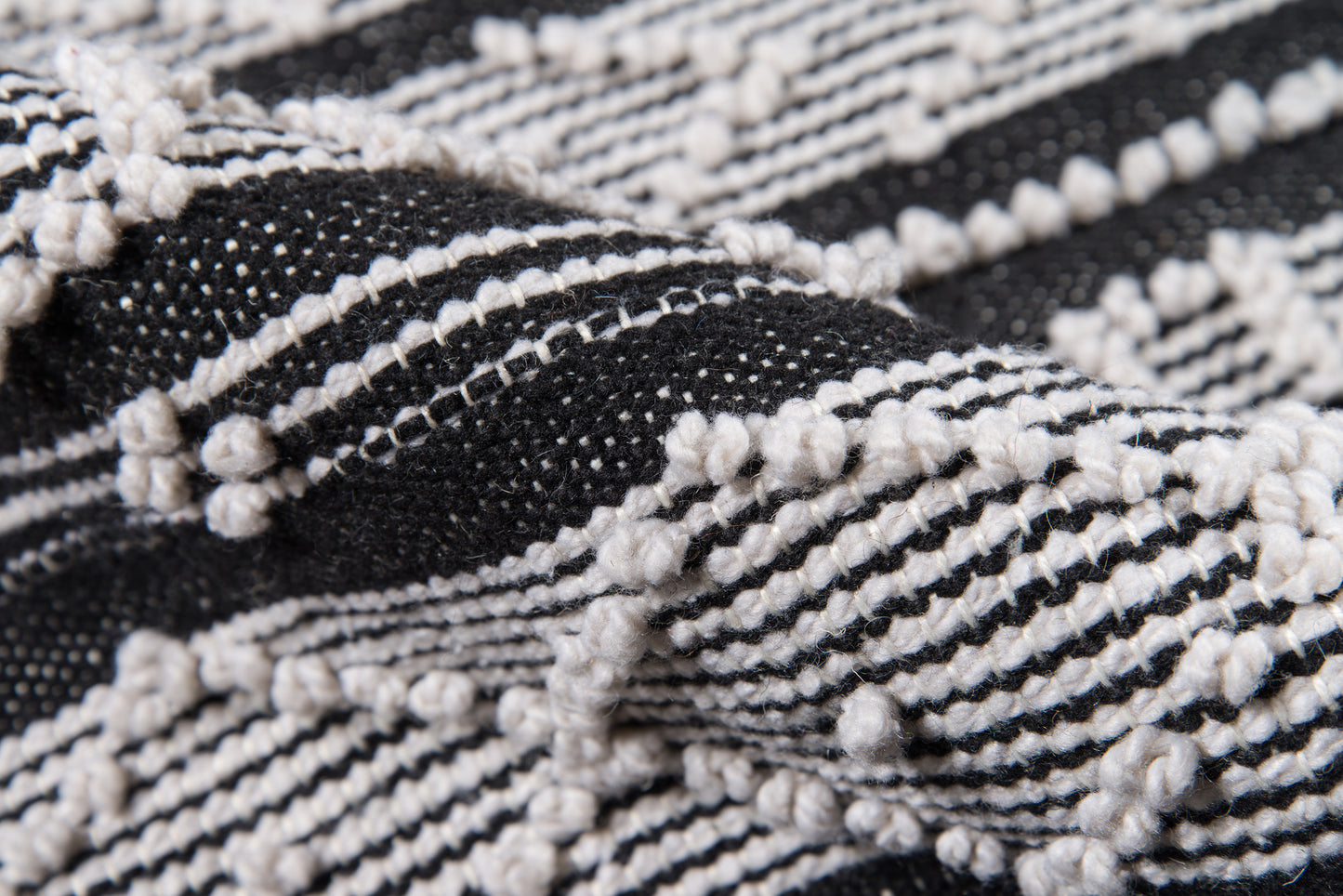 Close-up of black and white woven rug with raised loop knots and striped pattern.