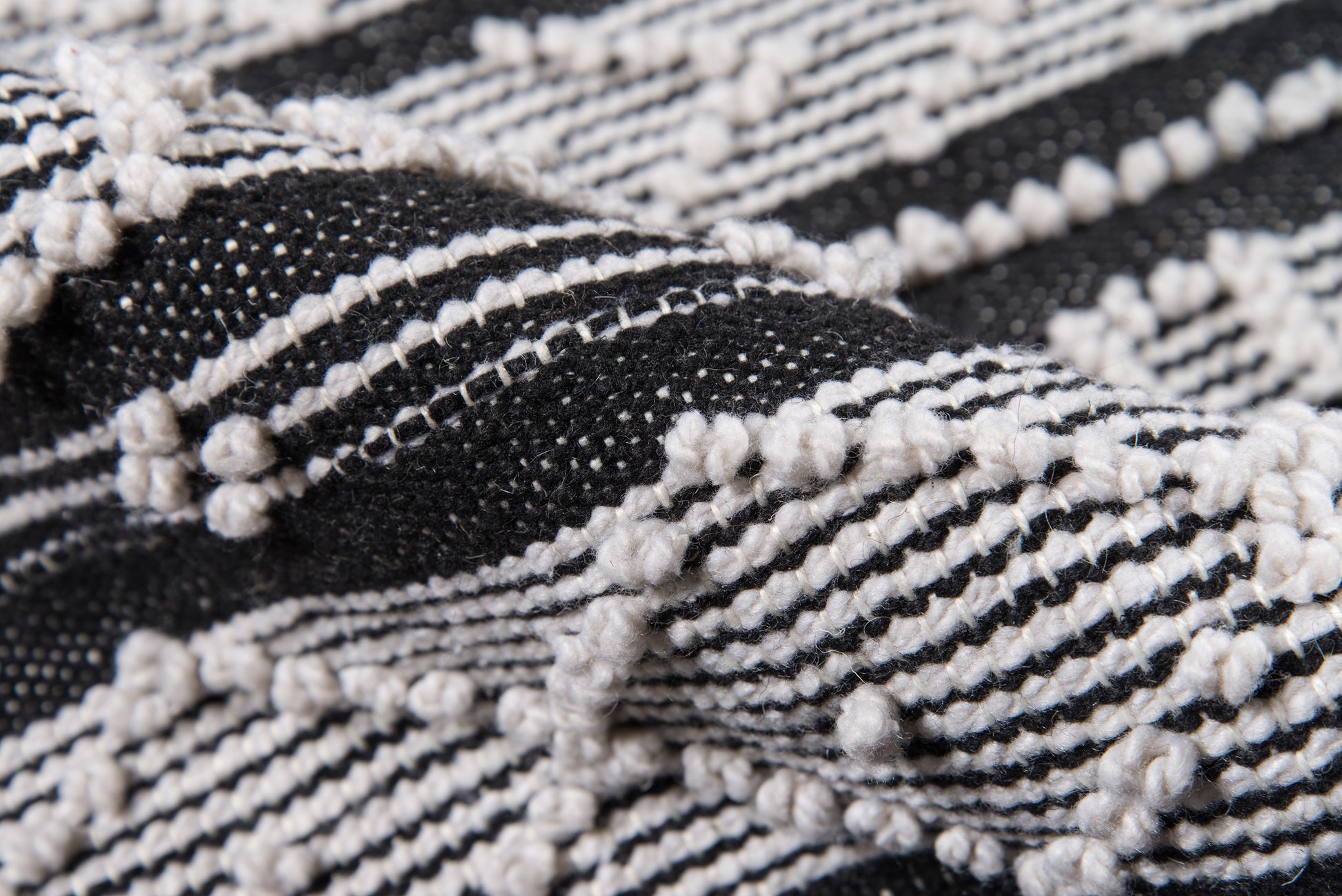 Close-up of black and white woven rug with raised loop knots and striped pattern.