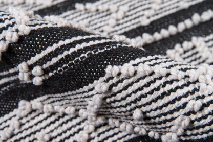Close-up of black and white woven rug with raised loop knots and striped pattern.