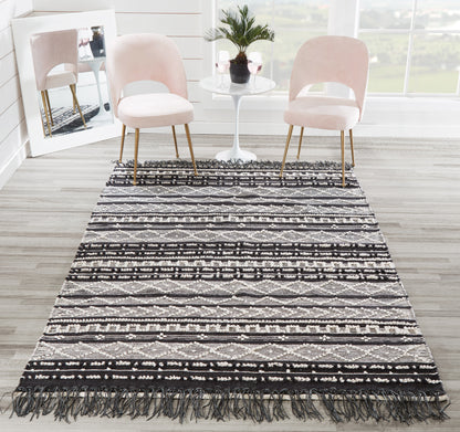 Geometric black and white area rug with fringe, paired with blush pink chairs and a white round table with a plant.