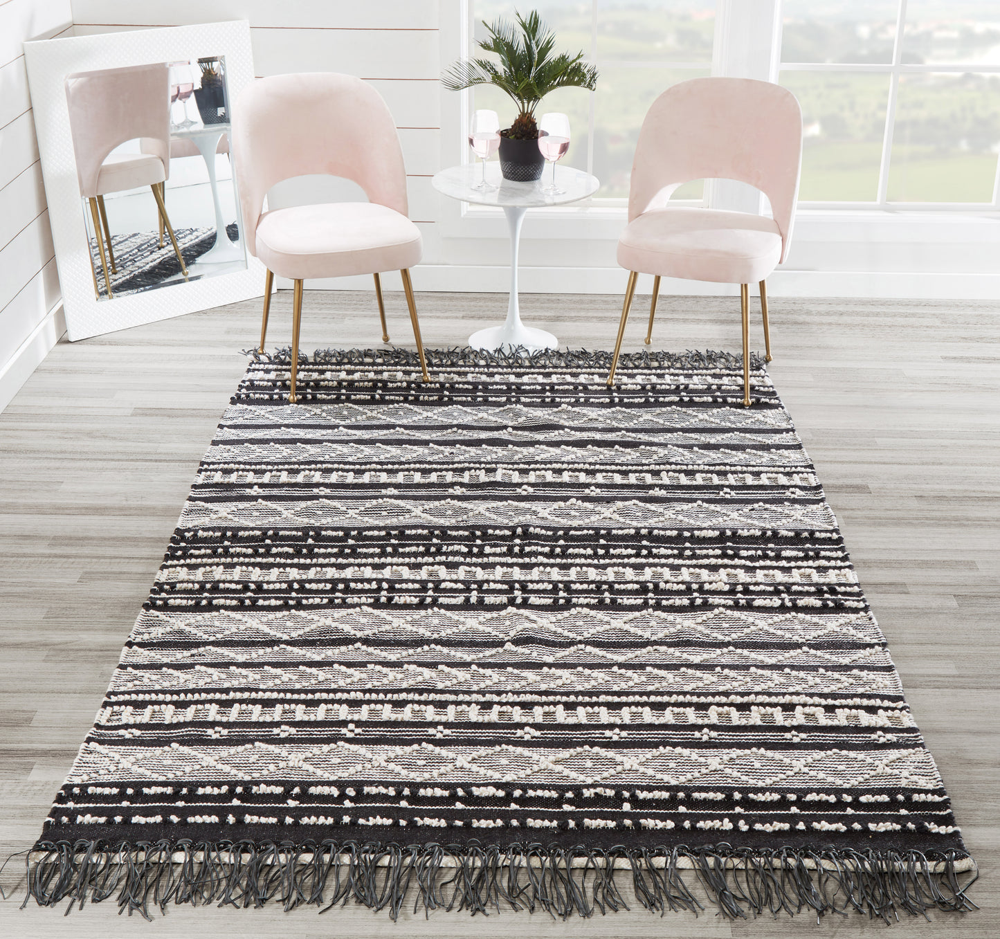 Blush pink rug with a long black-and-white geometric fringe; blush pink chairs flank a white round table placed on it.