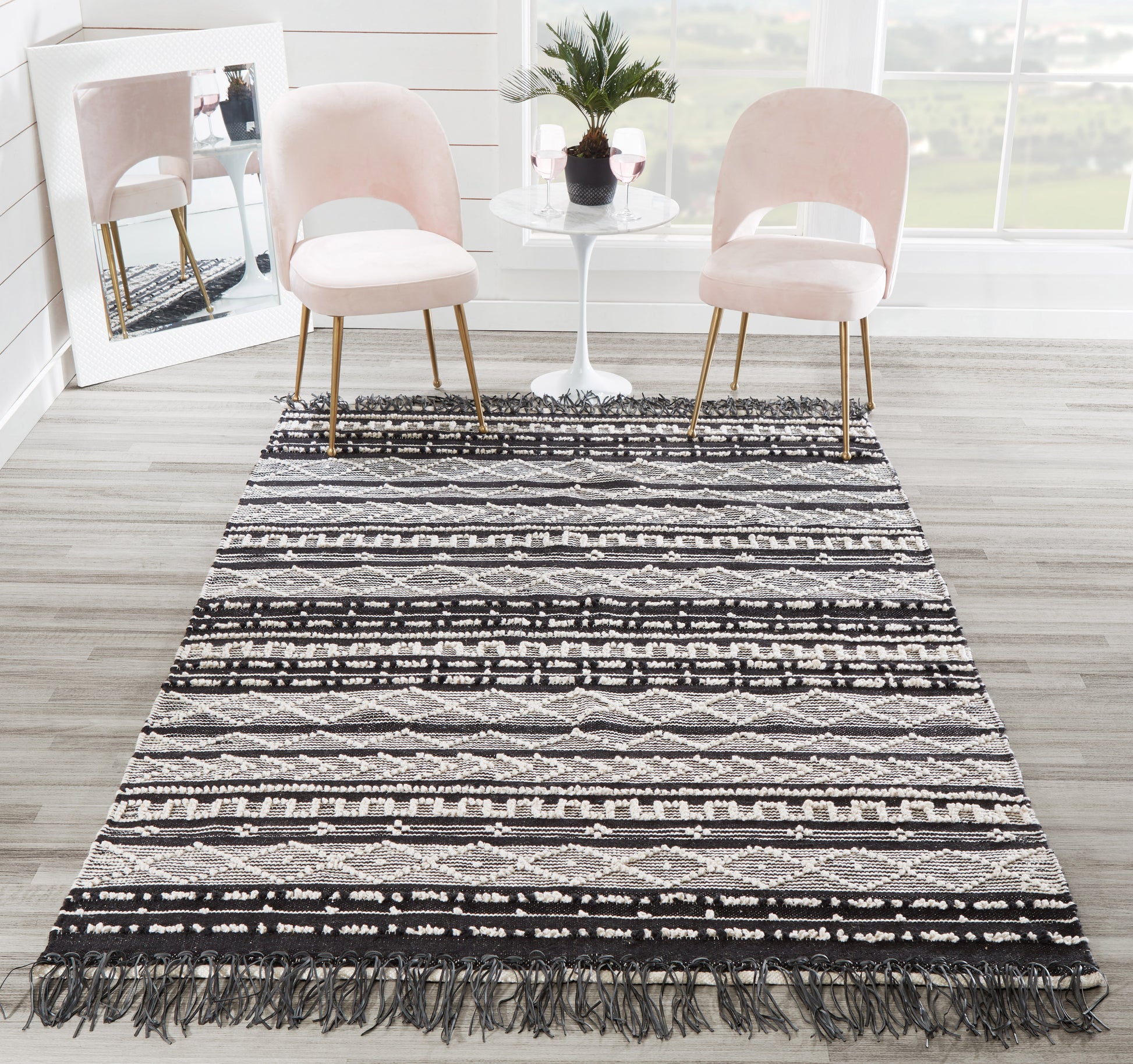 Blush pink rug with a long black-and-white geometric fringe; blush pink chairs flank a white round table placed on it.