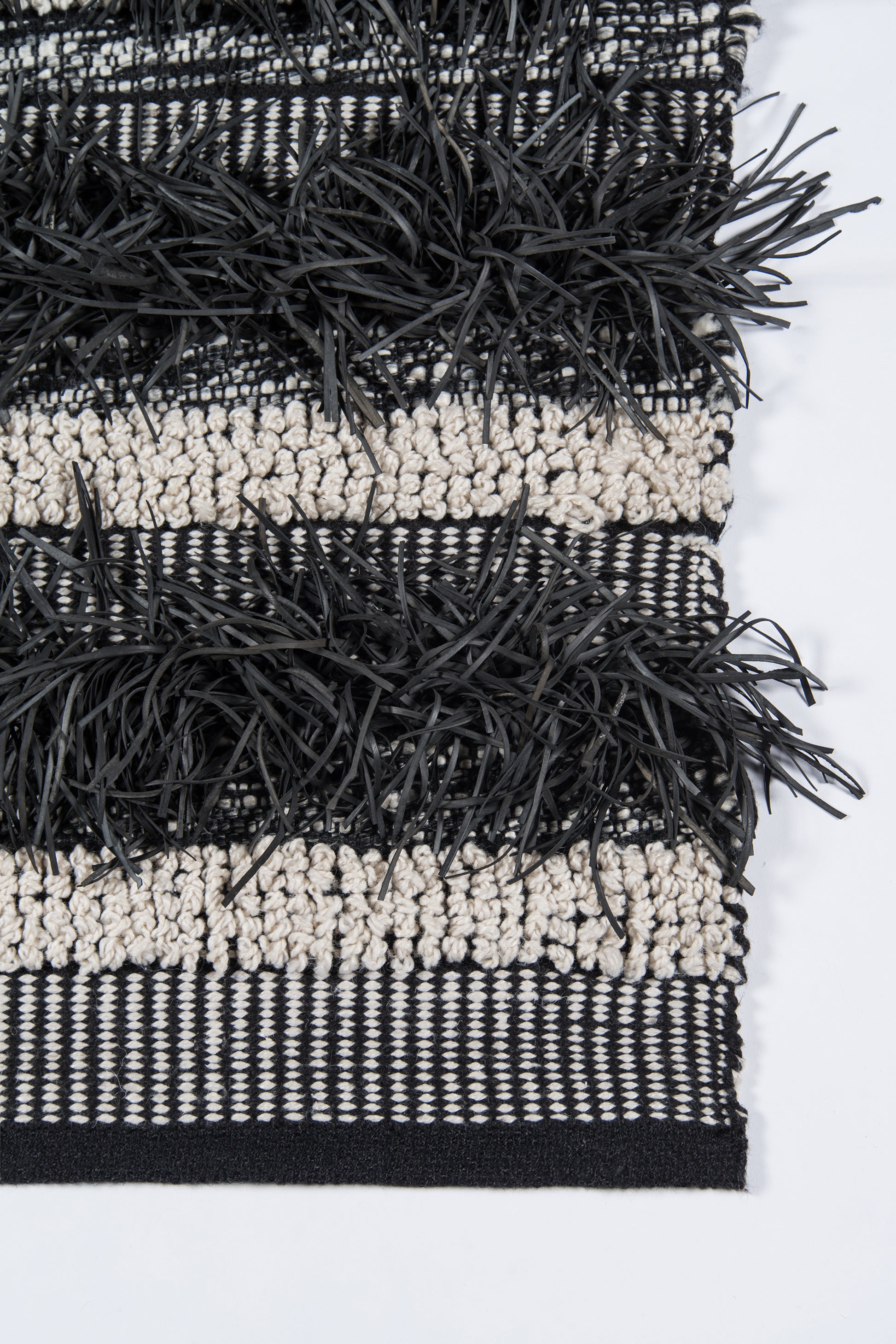 Woven rug in black and cream stripes with chunky black fringe trim.