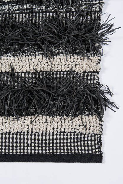 Woven rug in black and cream stripes with chunky black fringe trim.
