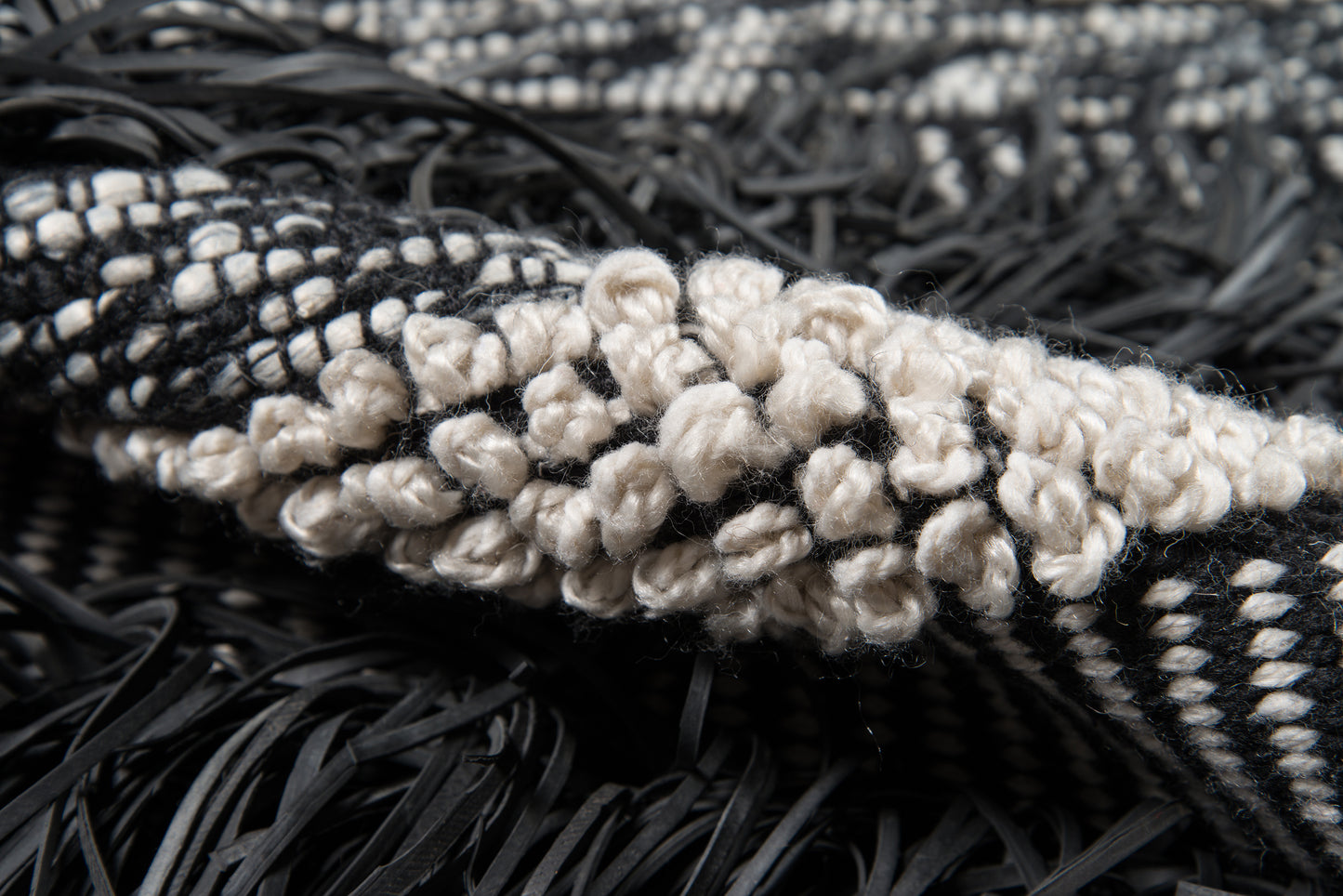 Close-up of a black-and-cream woven rug with chunky cream looped knots and black fringe.