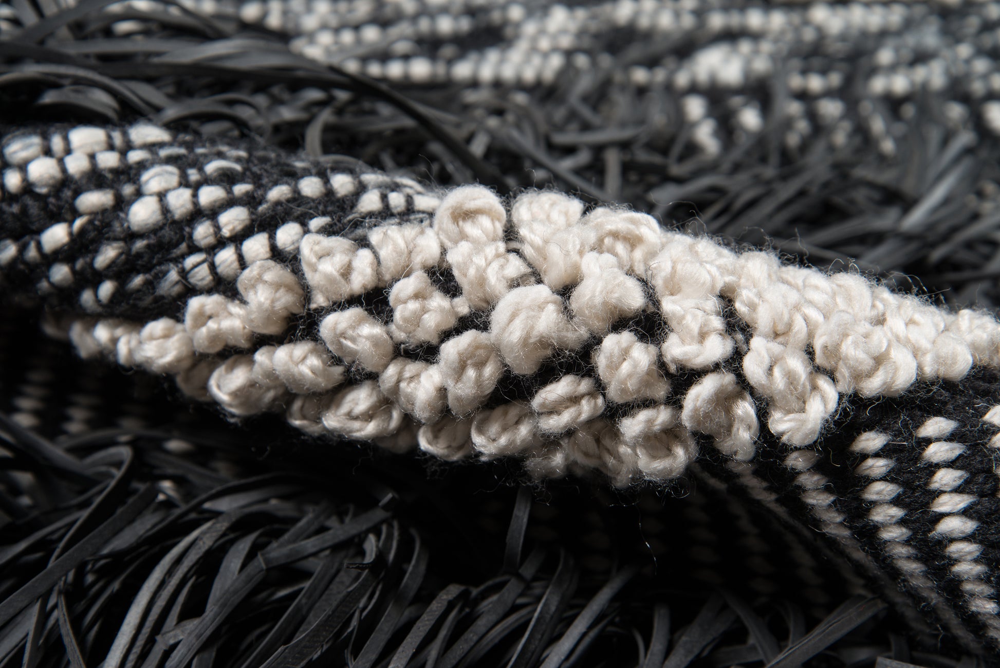 Close-up of a black-and-cream woven rug with chunky cream looped knots and black fringe.