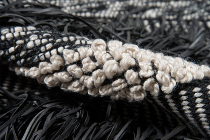 Close-up of a black-and-cream woven rug with chunky cream looped knots and black fringe.