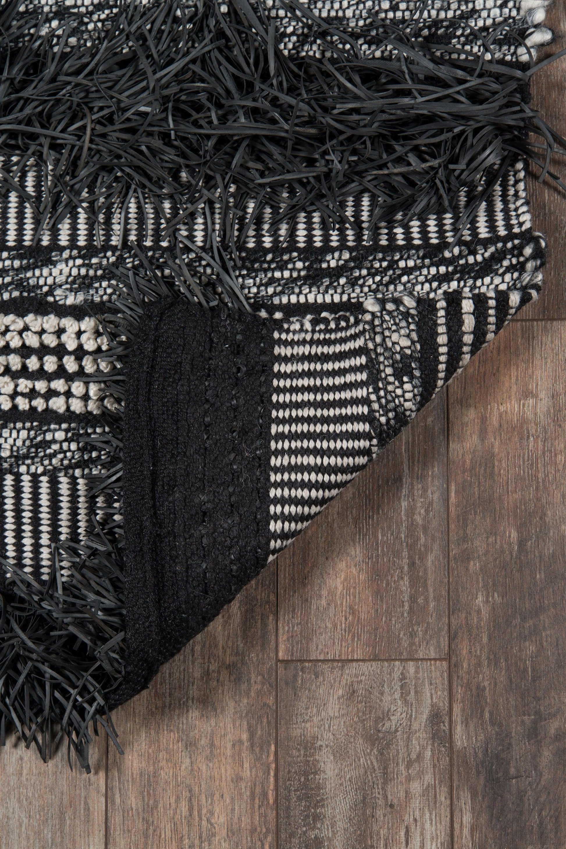 Black and white woven rug with fringed edges, draped on a wooden floor.