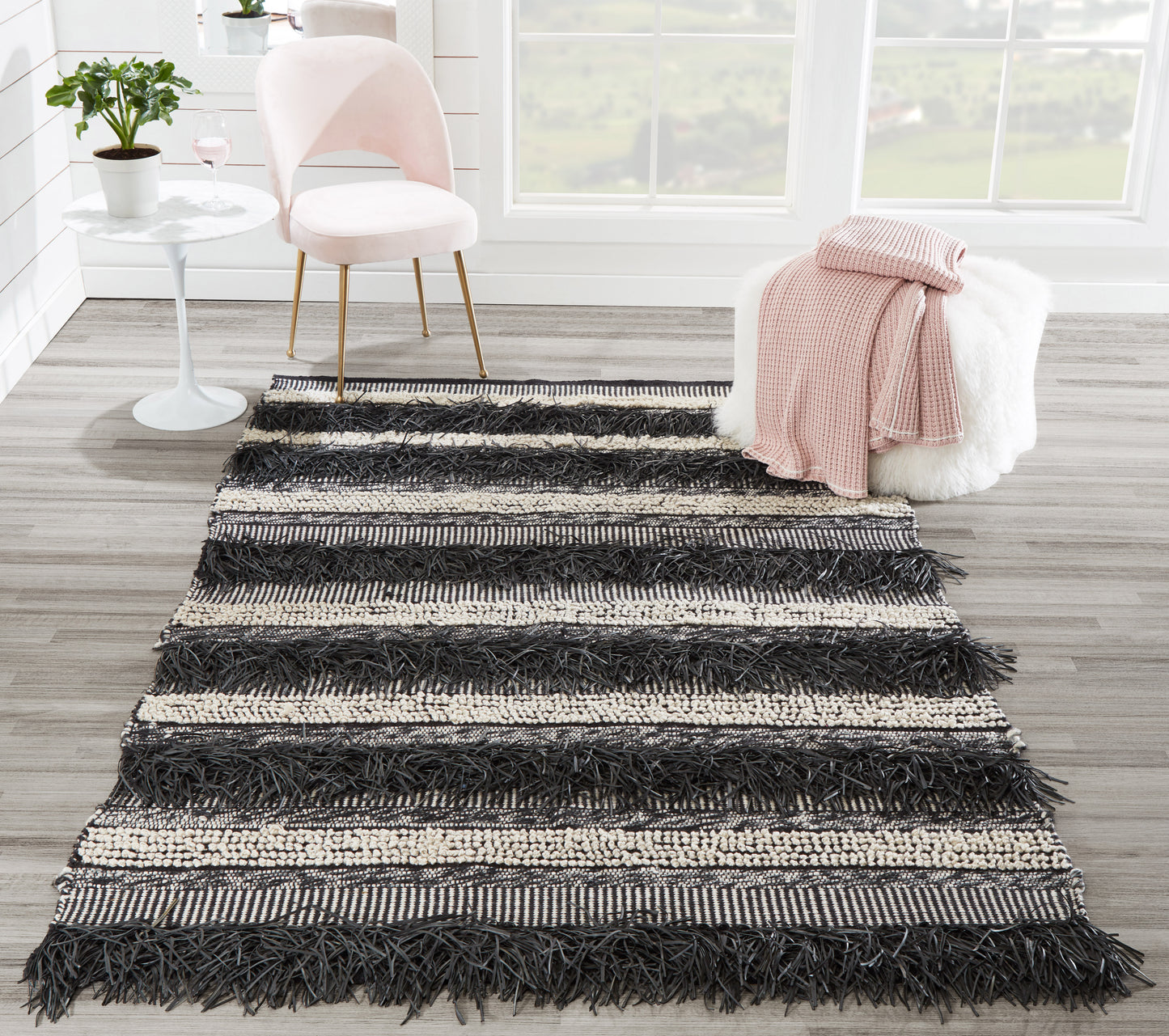 Rectangular black and cream striped shag rug with chunky fringe; boho living room decor on light wood floor.