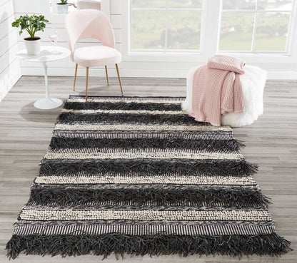 Rectangular black and cream striped shag rug with chunky fringe; boho living room decor on light wood floor.