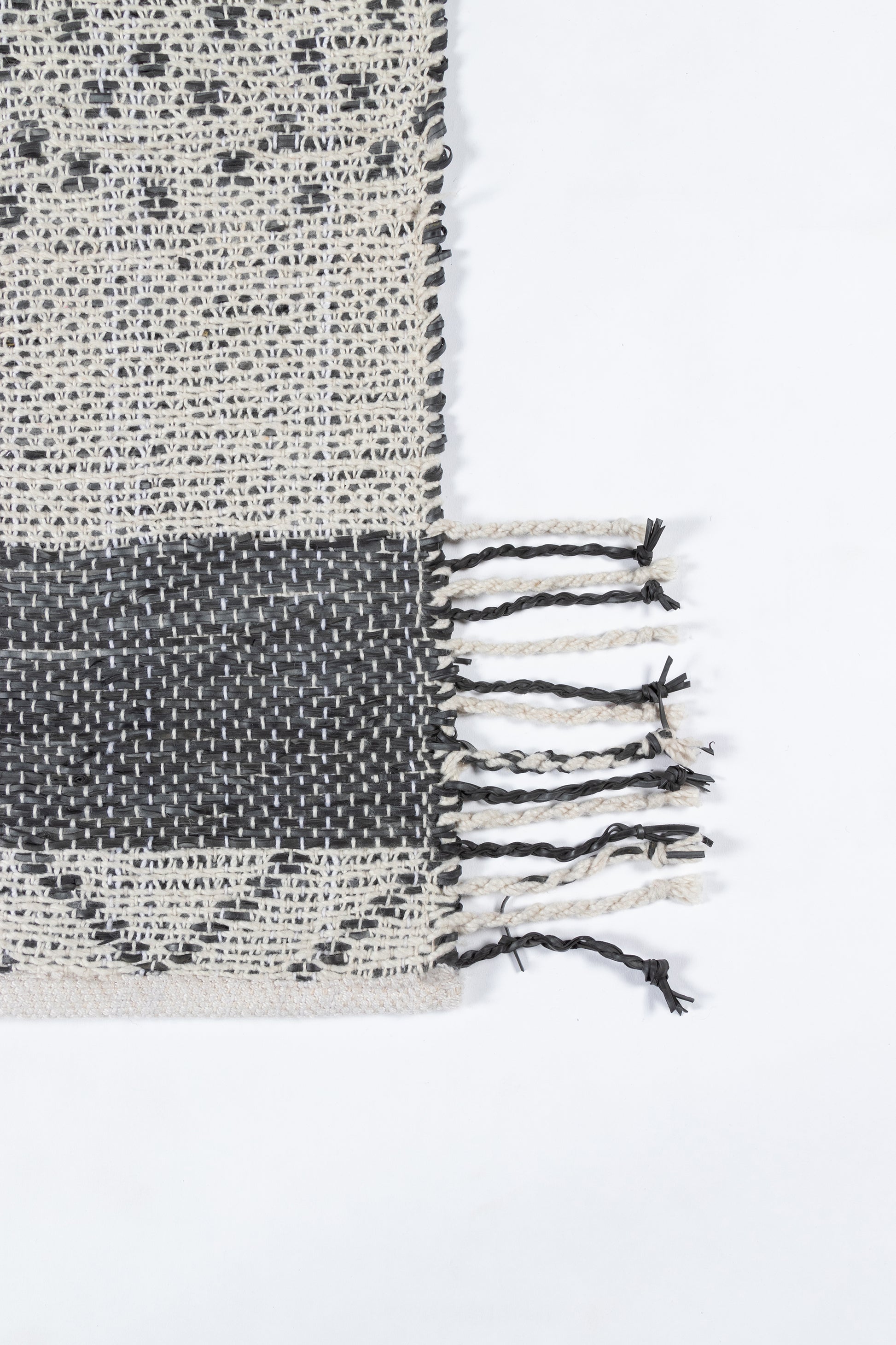 Beige and charcoal woven rug with a fringed edge and geometric pattern.