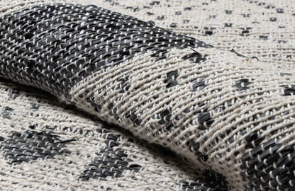 Folded black-and-cream woven rug with geometric pattern and chunky textured weave for modern boho home decor.