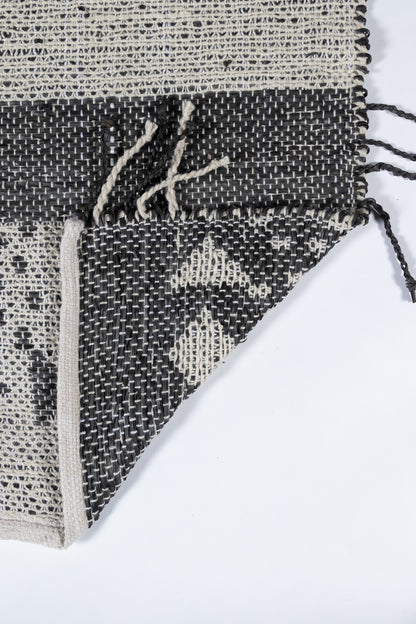 Woven rug in black and natural ivory with geometric diamond pattern and fringed edges