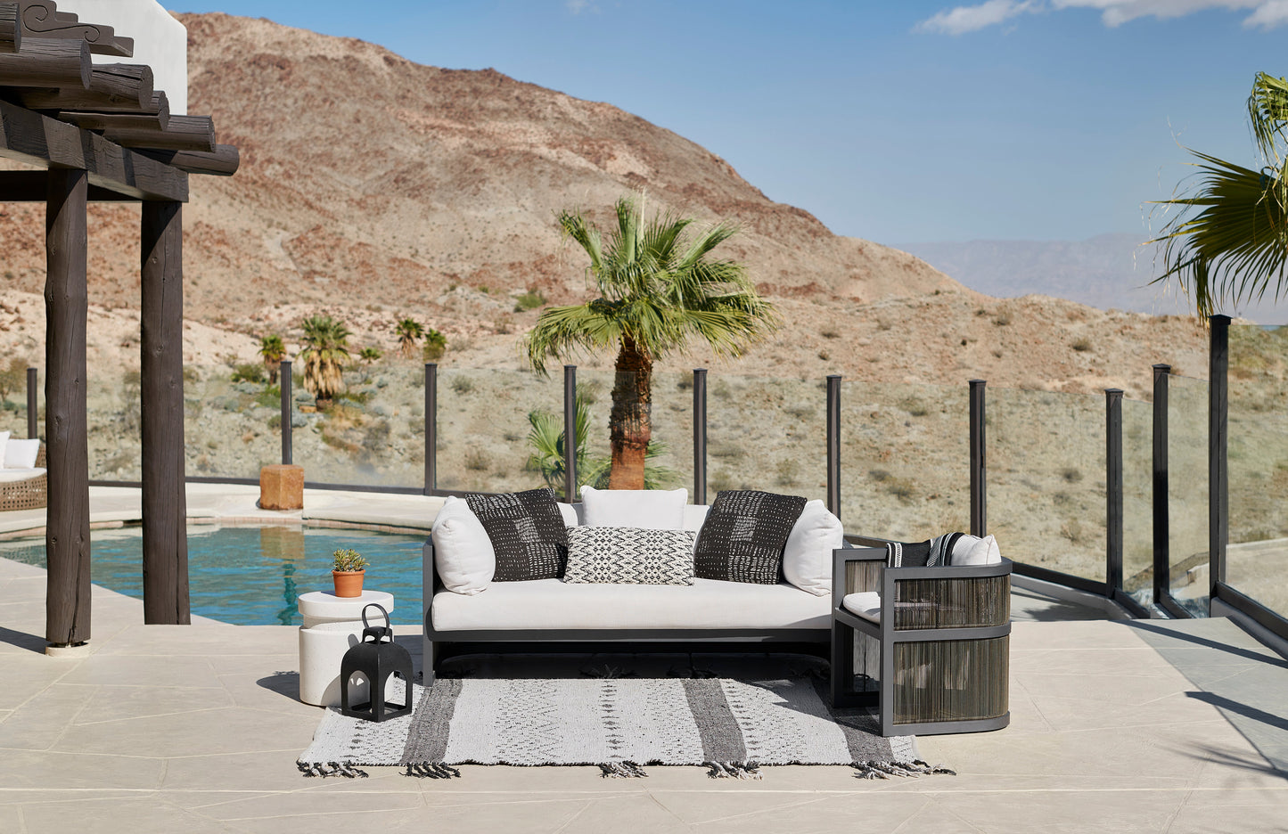 5' x 8' outdoor patio rug in black with a geometric pattern, on a poolside patio with desert hills in the background.