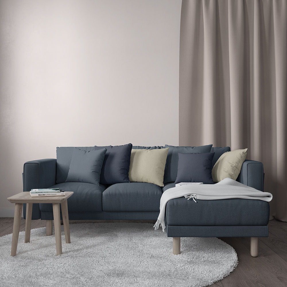 Blue-gray sectional sofa with chaise, navy & beige cushions, light wood legs, throw blanket; round coffee table & shag rug.