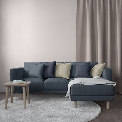 Blue-gray sectional sofa with chaise, navy & beige cushions, light wood legs, throw blanket; round coffee table & shag rug.