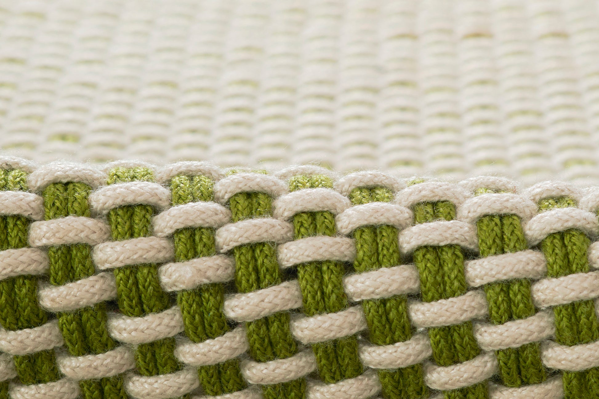 Close-up of beige and olive-green woven rug fibers with chunky interlaced threads forming a checker-like pattern.