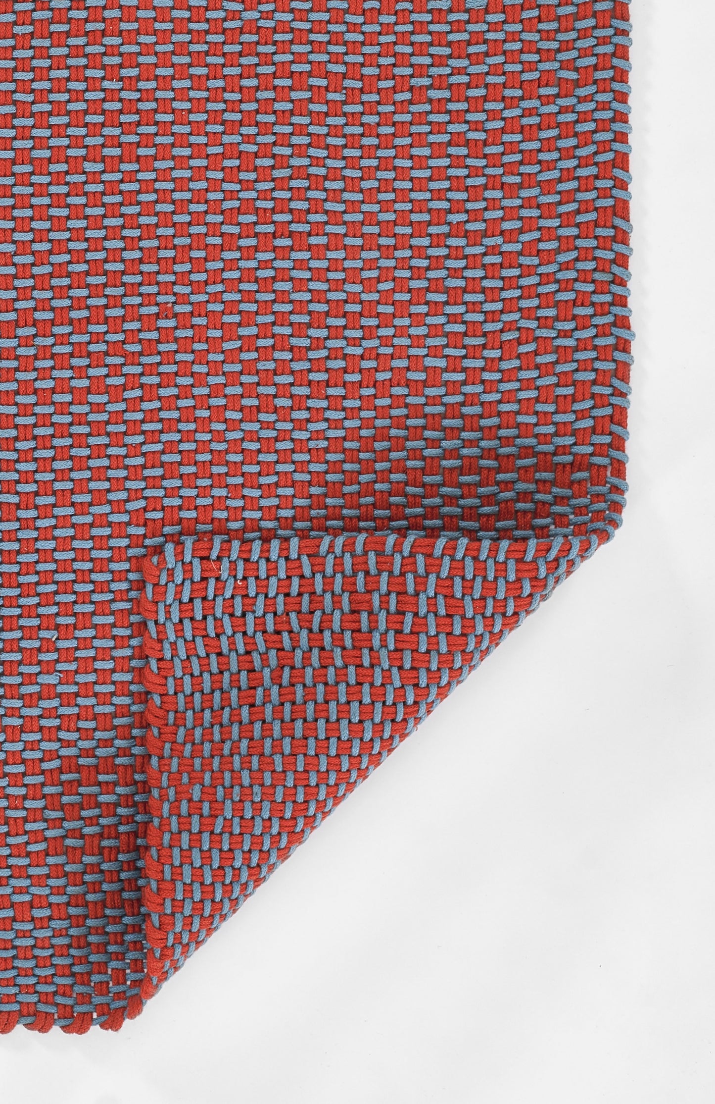 Red and blue woven rug runner with a small grid pattern, rectangular with a folded corner.